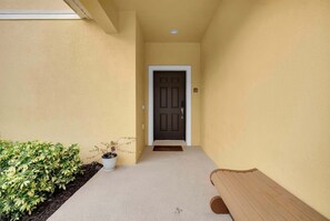 Un couloir étroit, avec une porte au fond, un petit banc et une plante en pot.