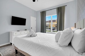 A hotel room with a bed, a TV mounted on the wall, a dresser, and a window with curtains. - Paradise Palms Family Oasis (Kissimmee)