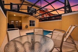A poolside area with a round table and chairs, a pool, and a view of a building with a balcony. - Paradise Palms Family Oasis (Kissimmee)