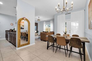 A modern kitchen with a dining area, featuring a large mirror, a chandelier, and a view into the living room. - Paradise Palms Family Oasis (Kissimmee)