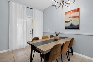 A dining area with a long table, six chairs, a chandelier, and a painting on the wall. - Paradise Palms Family Oasis (Kissimmee)