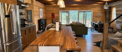 Una cocina moderna con un refrigerador de acero inoxidable, armarios de madera y una barra de madera larga con taburetes.