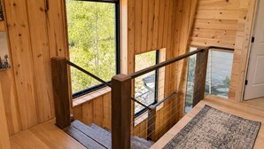 Een houten interieur met een trap, een raam met uitzicht op bomen, en een deur.