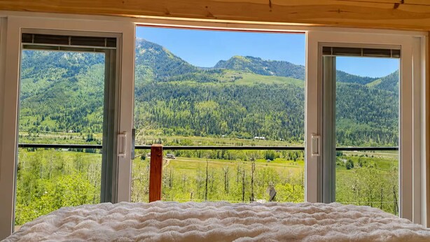Een kamer met een bed en uitzicht op een bergachtig landschap door open deuren.