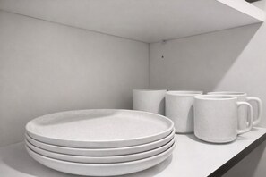 A stack of white plates and mugs on a white shelf. - Modern 1BR Near Downtown Atlanta Pool, Gym & Balcony (Atlanta)