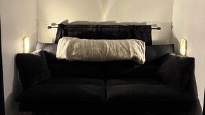 En mørk sofa med et tæppe, to sengeborde med lamper og en loftlampe.
