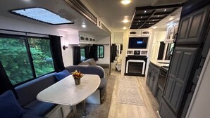 En kompakt indretning i en autocamper med spiseplads, siddepladser, et køkken og et fjernsyn.