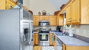 Una cocina con armarios de madera, electrodomésticos de acero inoxidable, microondas, horno y un lavamanos.