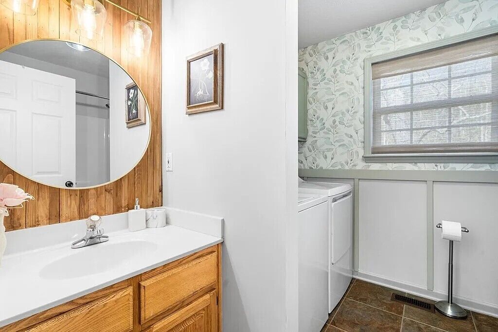 Une salle de bain avec un meuble-lavabo en bois, un grand miroir, des toilettes et une fenêtre.
