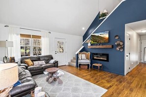 Una sala de estar con chimenea, escalera y vistas al exterior.