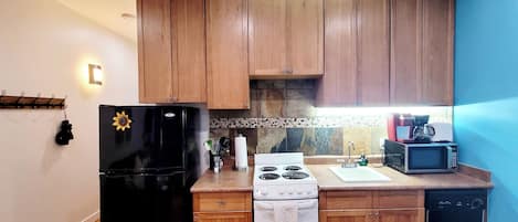 Una cocina compacta con armarios de madera, un refrigerador negro, una estufa blanca, un microondas y un lavavajillas.