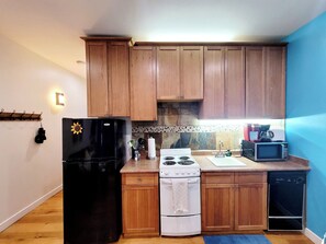 Una cucina compatta con mobili in legno, un frigorifero nero, un fornello bianco, un forno a microonde ed una lavastoviglie.