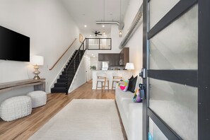 A modern living room with a staircase, a kitchen, and a large TV. - Hub City Retreat (Lubbock)