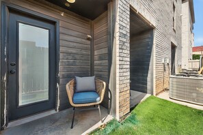A modern building exterior with a dark door, a wicker chair with a cushion, and a small grassy area. - Hub City Retreat (Lubbock)