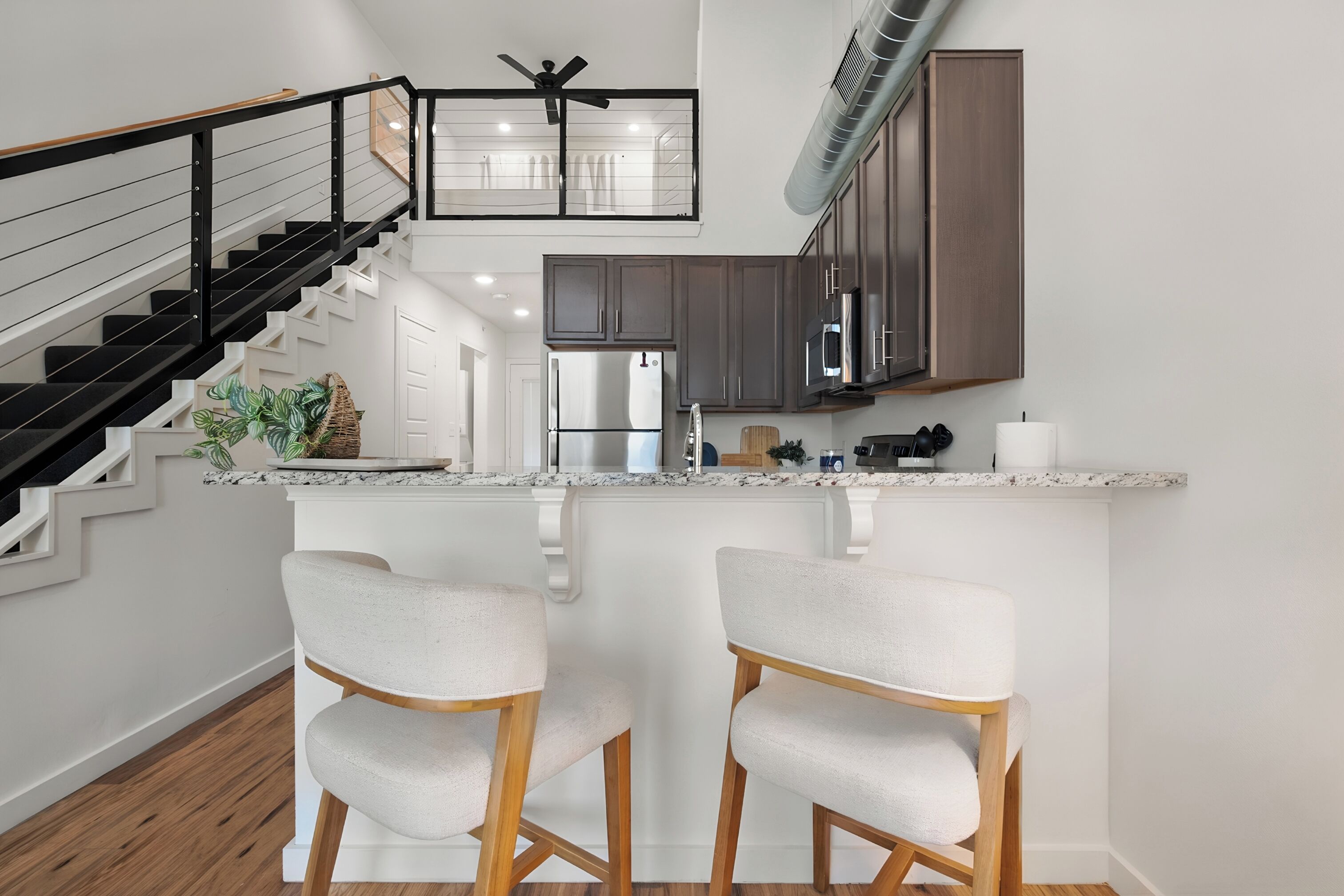 Une cuisine moderne dotée d’un îlot central, d’appareils électroménagers en acier inoxydable et d’un escalier avec des rampes noires.