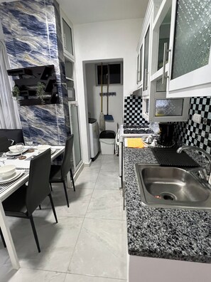 Eine schmale Küche mit Essbereich, Granit-Arbeitsplatten, einer Edelstahl-Spüle und einer karierten Spritzschutzwand.