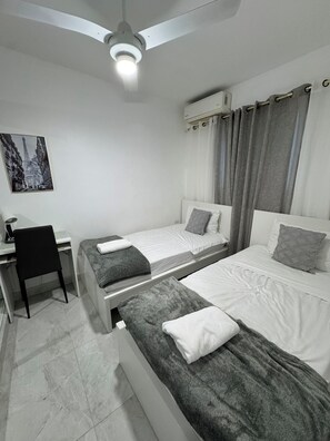 A bedroom with two beds, a desk, a chair, a ceiling fan, and an air conditioning unit. - Res. Christall 1, Apartment 2-A, with a view of the mountains  (Santiago de los Caballeros)