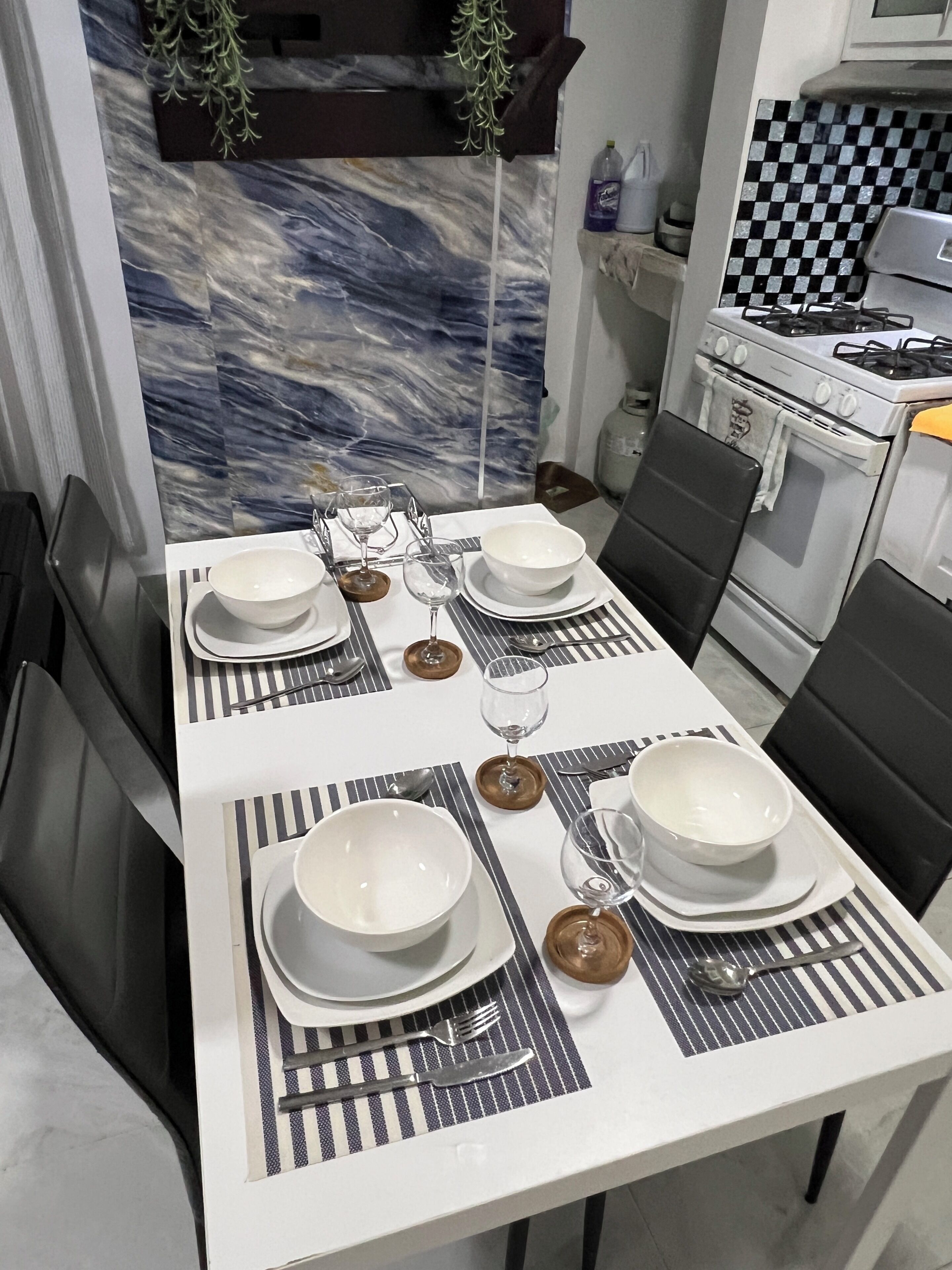 Comedor con una mesa dispuesta para cuatro personas, incluyendo platos, tazones, vasos y cubiertos.