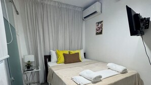 Ein Hotelzimmer mit einem Bett, einem Nachttisch mit Lampe, einem Wand-Fernseher und einer Klimaanlage.