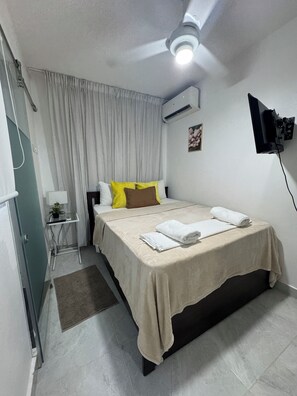 Ett hotellrum med en säng, ett sängbord med en lampa, en väggmonterad TV och en luftkonditioneringsanläggning.