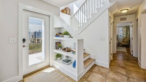 Een modern interieur met een trap naar een tweede verdieping, een deur met uitzicht naar buiten, en een gang met een bank en gordijnen.