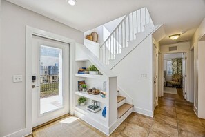 A modern interior with a staircase leading to a second floor, a door with a view to the outside, and a hallway with a bench and curtains. - Renovated and Spacious 6BR duplex on Amelia Island near the beach with pool (Fernandina Beach)