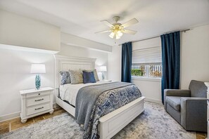 A bedroom with a bed, bedside tables, a chair, a ceiling fan, and a window with curtains. - Renovated and Spacious 6BR duplex on Amelia Island near the beach with pool (Fernandina Beach)