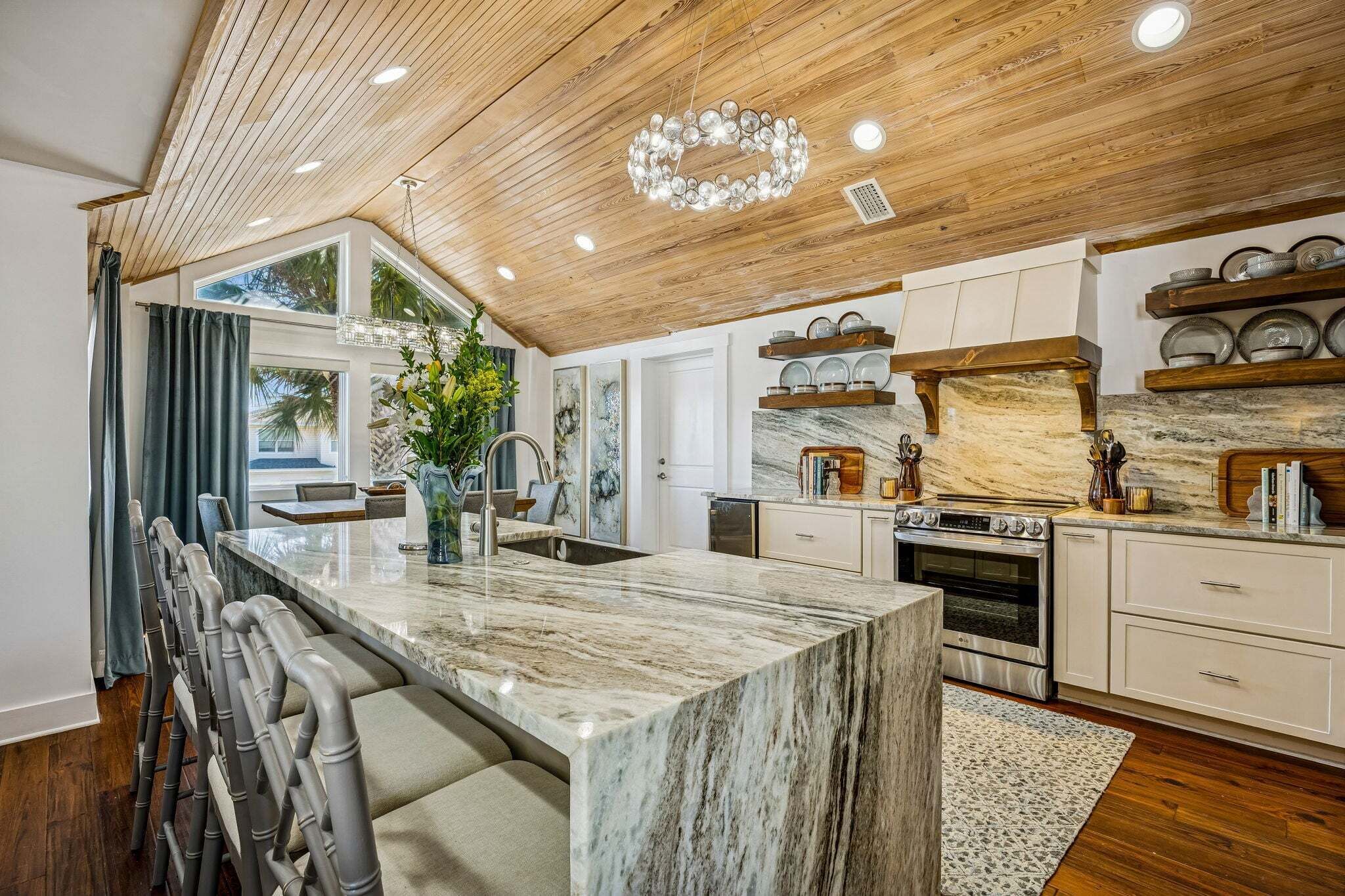 Een moderne keuken met een marmeren eiland, een houten plafond en inbouwapparatuur.