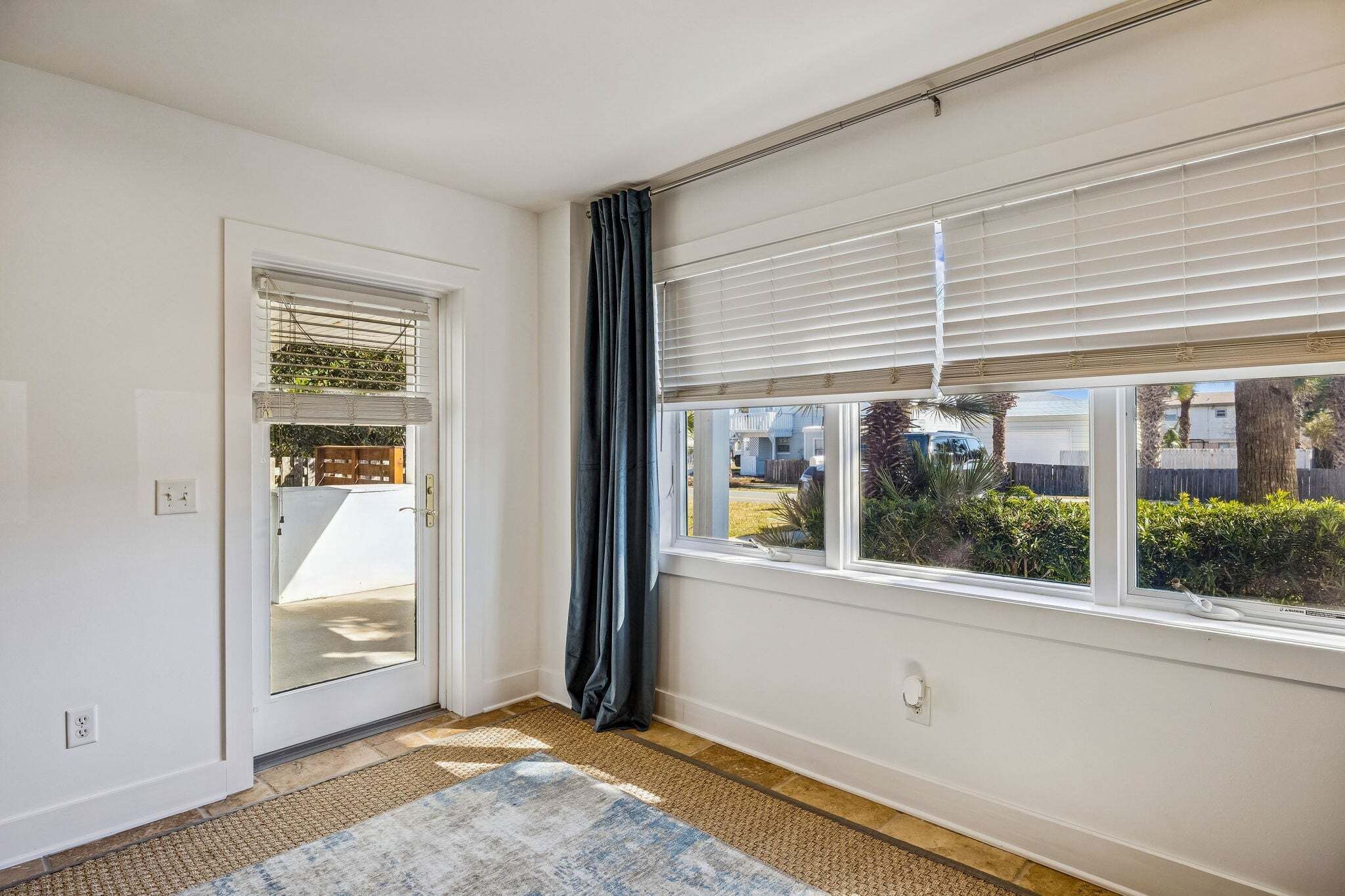Ein Zimmer mit einer zur Außenseite führenden Tür, einem mit Jalousien versehenen Fenster und einem Teppichboden.