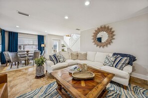 A modern living room with a sectional sofa, a coffee table, and a dining area with chairs. - Renovated and Spacious 6BR duplex on Amelia Island near the beach with pool (Fernandina Beach)