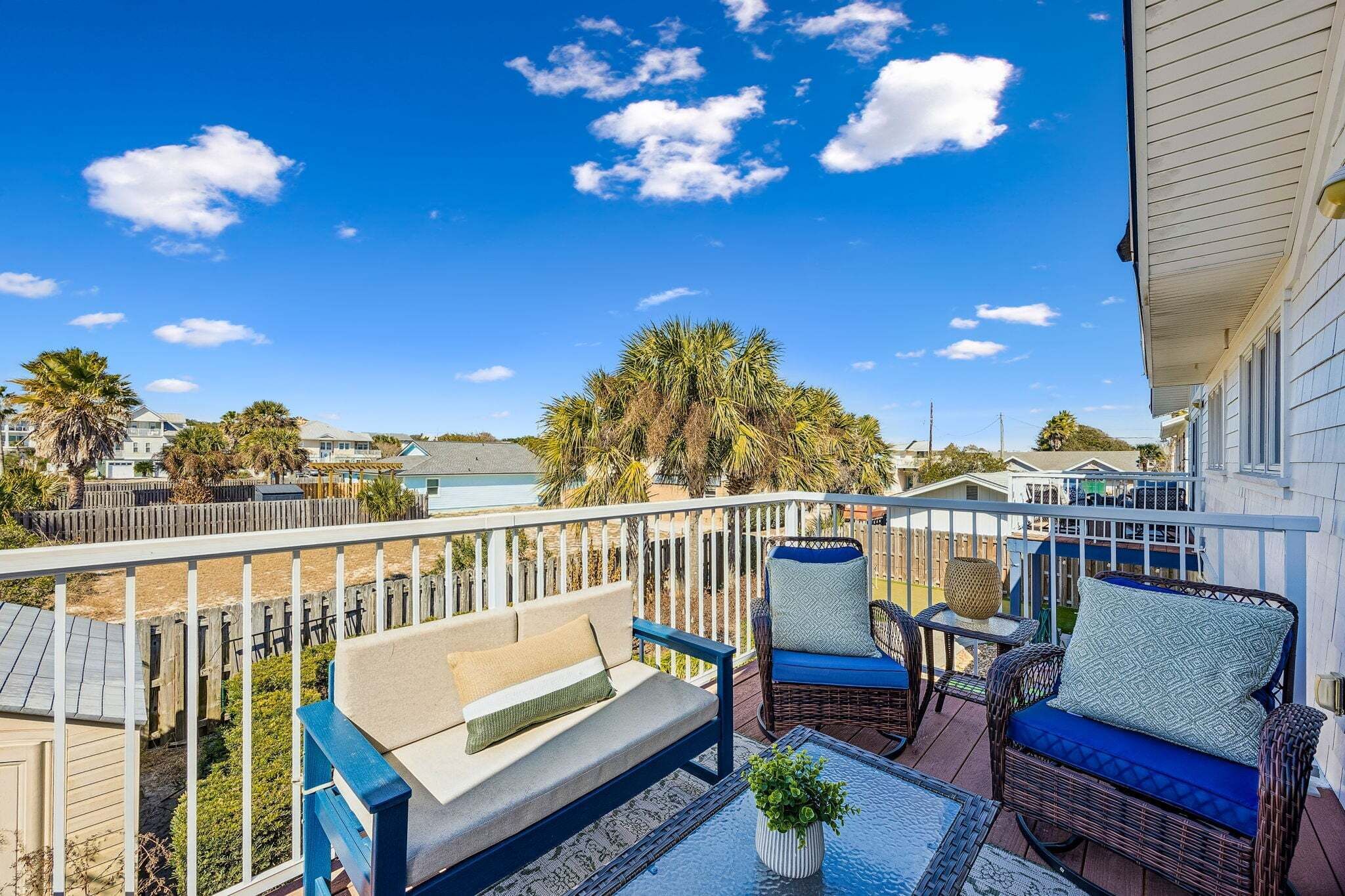 Een balkon met tuinmeubilair, uitzicht op zee en een houten omheining.