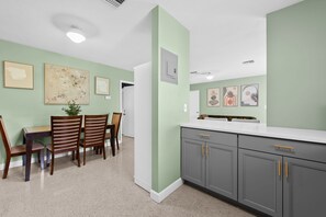 A modern kitchen with a dining area, featuring a white countertop, grey cabinets, and a green accent wall. - Sunny 2BR Apartment w/ Private Backyard & Hot Tub (Wilton Manors)