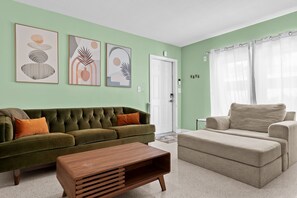 A living room with a green sofa, a beige sofa, and a wooden coffee table. There are three framed artworks on the wall. - Sunny 2BR Apartment w/ Private Backyard & Hot Tub (Wilton Manors)