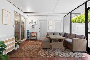Eine sonnendurchflutete Terrasse mit einem Korbsessel, einem Holztisch und einem gemusterten Teppich.