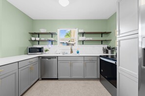 A modern kitchen with grey cabinets, a dishwasher, a microwave, and a refrigerator. - Sunny 2BR Apartment w/ Private Backyard & Hot Tub (Wilton Manors)