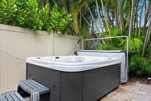 A hot tub in a backyard with a wooden fence, a metal chair, and various plants. - Sunny 2BR Apartment w/ Private Backyard & Hot Tub (Wilton Manors)