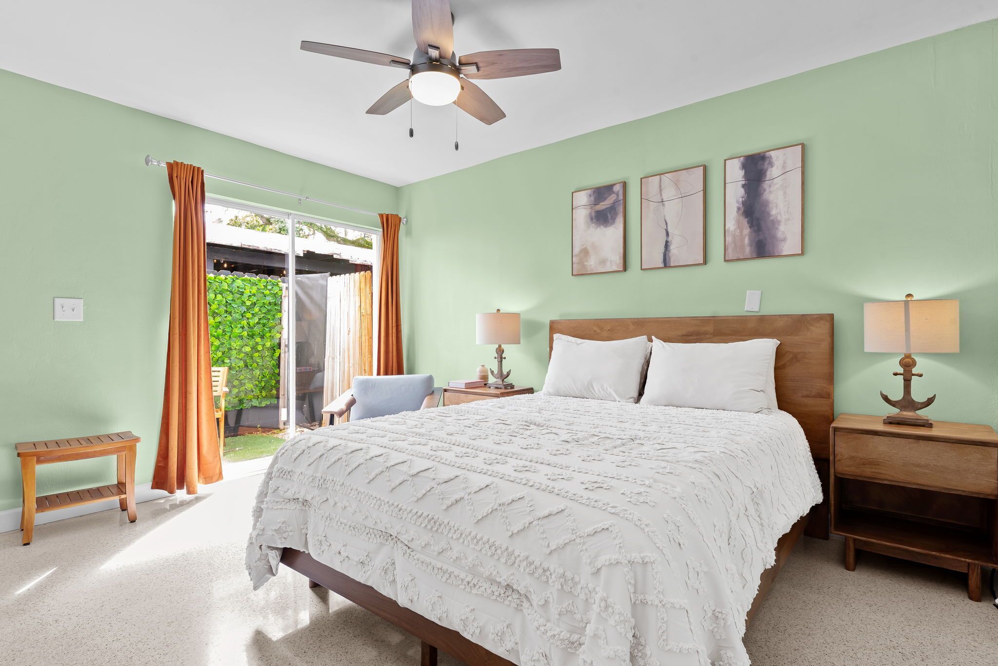 Un dormitorio con cama, dos mesitas de noche, ventilador de techo y vista al exterior.