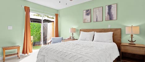 Un dormitorio con cama, dos mesitas de noche, ventilador de techo y vista al exterior.