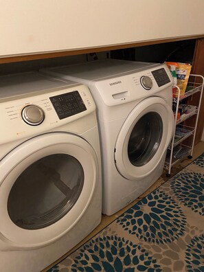 A laundry area with two white Samsung washing machines under a wooden cabinet.