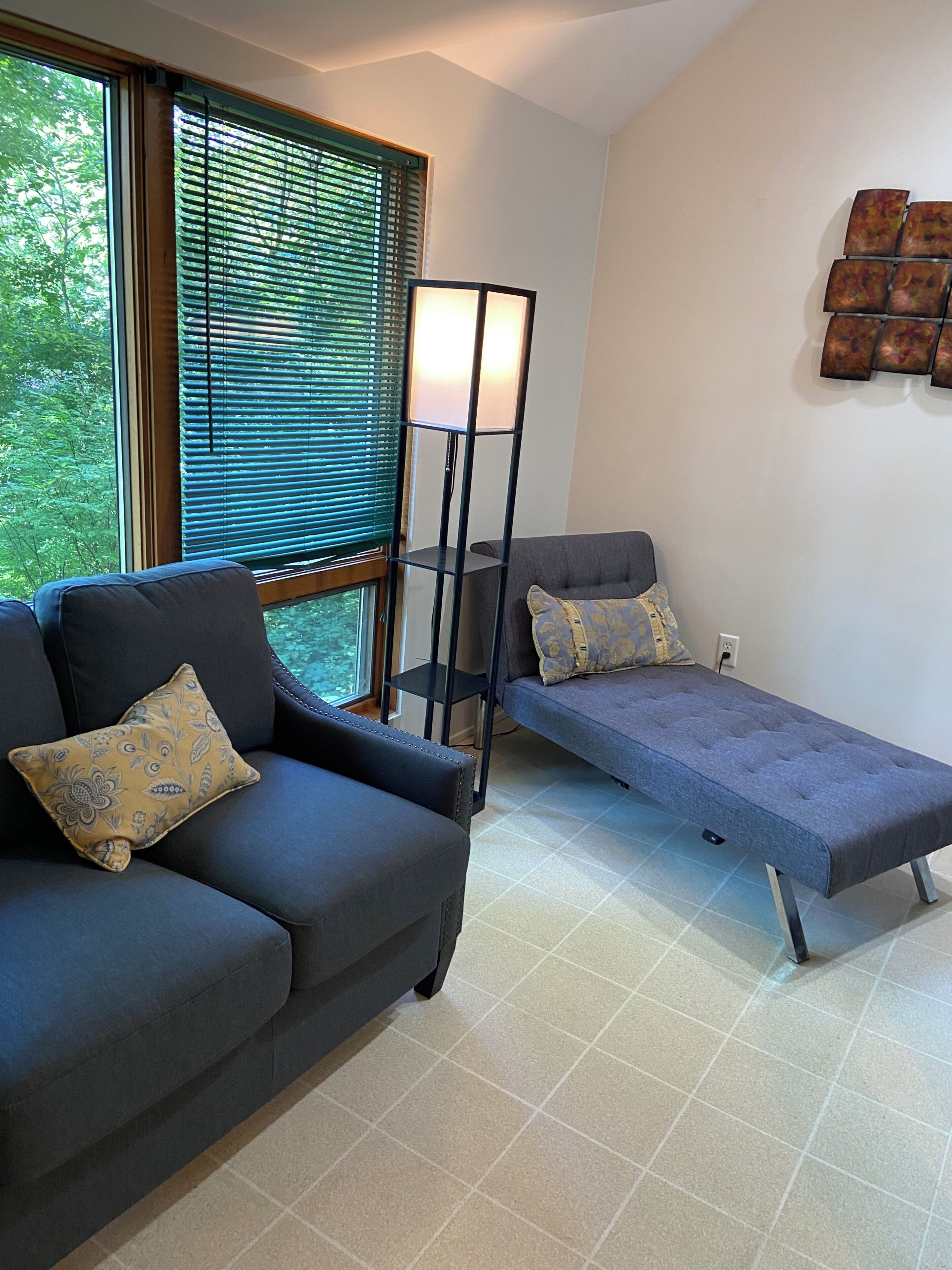 A modern living room with a sofa, a bench, a floor lamp, and a window with blinds.