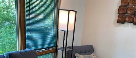 A modern living room with a sofa, a bench, a floor lamp, and a window with blinds.