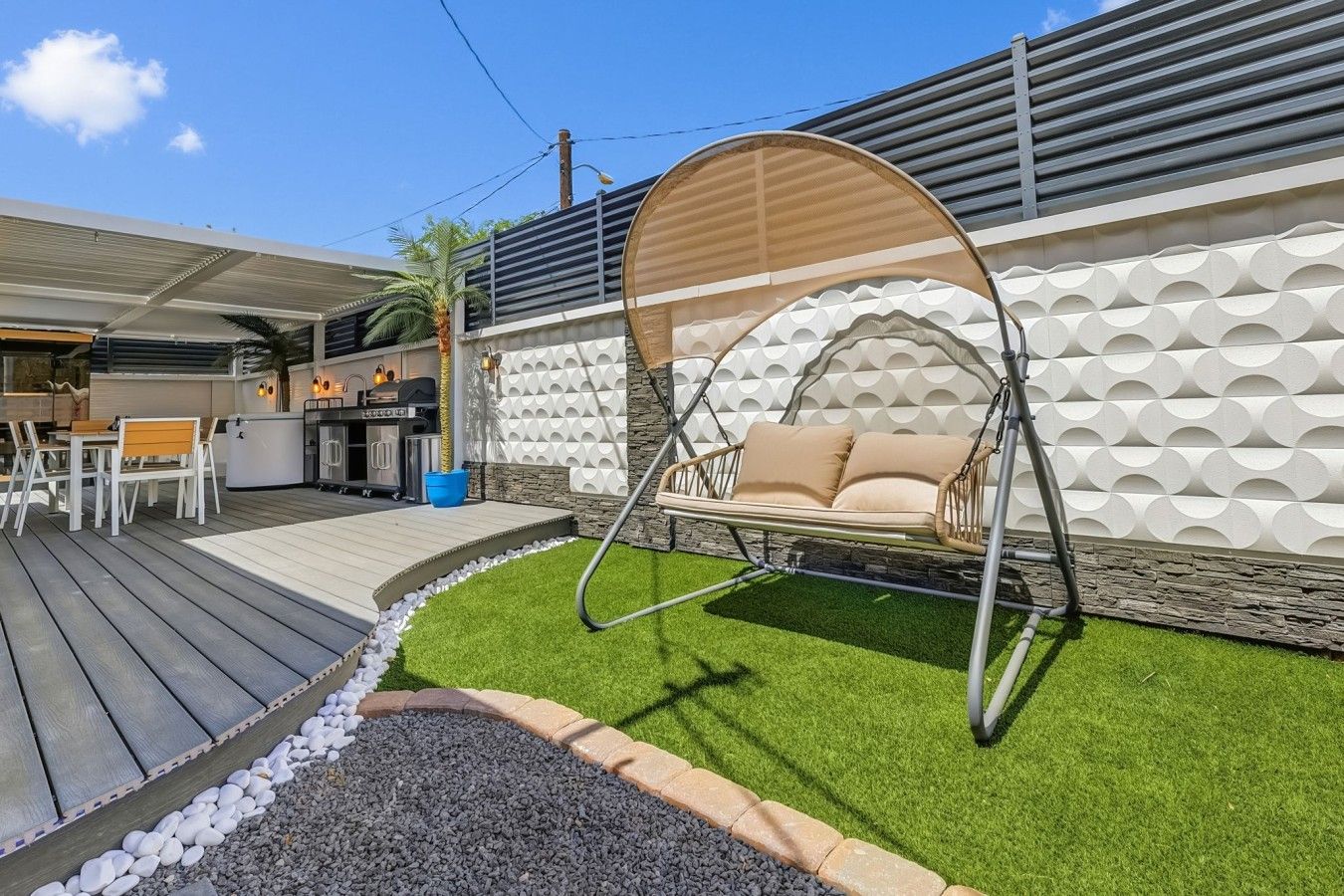 A patio with a swing chair, a barbecue area, and a stone wall with a geometric pattern.