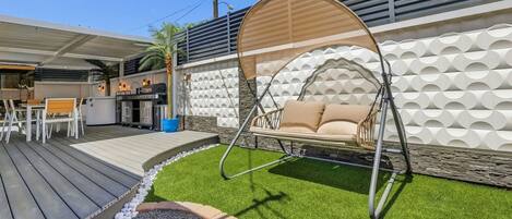 A patio with a swing chair, a barbecue area, and a stone wall with a geometric pattern.