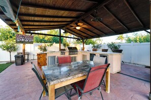 An outdoor patio with a barbecue grill, seating area, and a covered space with a ceiling fan. - West Covina Getaway, Pool & Game Room Near Disney (West Covina)