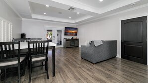 Uma sala de estar espaçosa com uma mesa de jantar, um sofá cinza e uma porta de madeira escura.