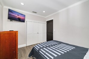 A bedroom with a bed, a dresser, a TV mounted on the wall, and a door. - West Covina Getaway, Pool & Game Room Near Disney (West Covina)