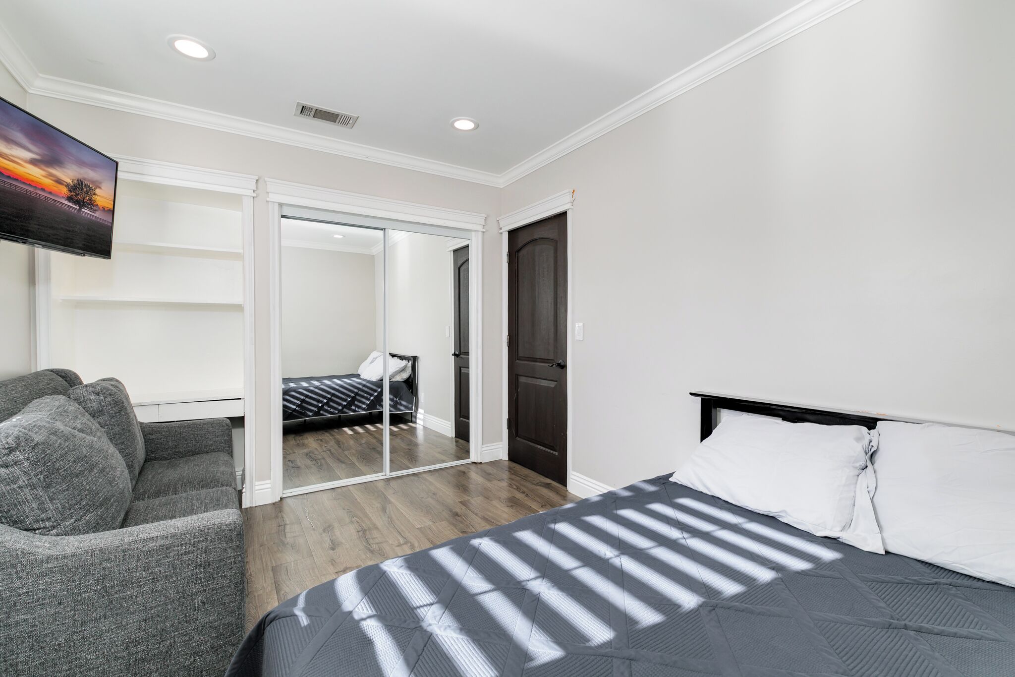 A hotel room with a bed, a seating area, a television, and a sliding door leading to a bathroom.