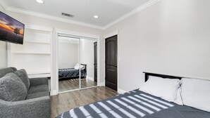 Quarto de hotel com cama, área de estar, televisão e porta de correr para um banheiro.