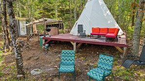 Ein Tipizelt mit roter Veranda, zwei Stühle mit gemusterten Kissen und einem Grill.