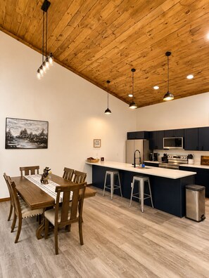 Une cuisine moderne avec un plafond en bois, un coin repas avec une table et des chaises, et un îlot de cuisine avec des tabourets.